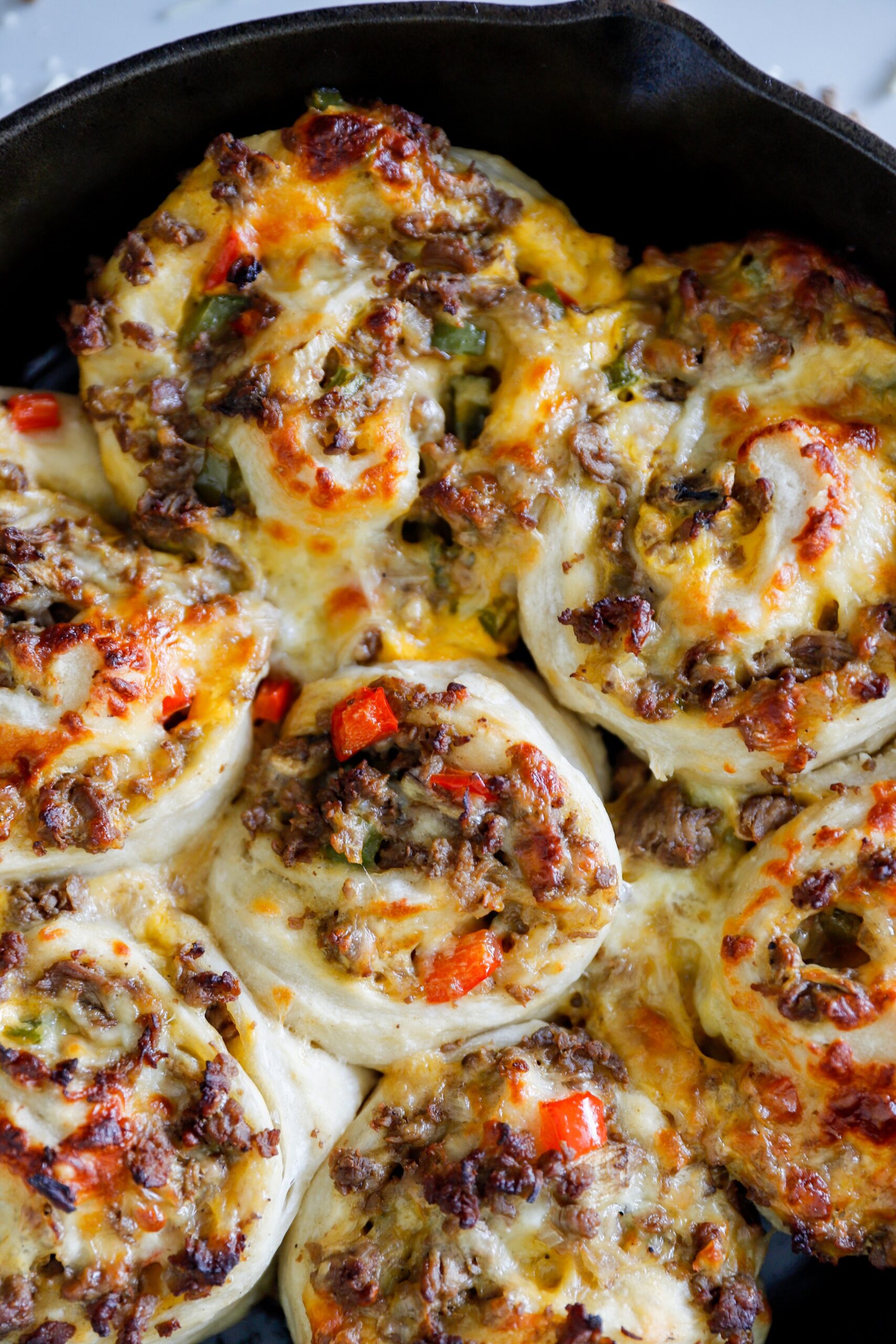 Close-up of crispy pinwheels, showing layers of steak, peppers, onions, and cheese inside.