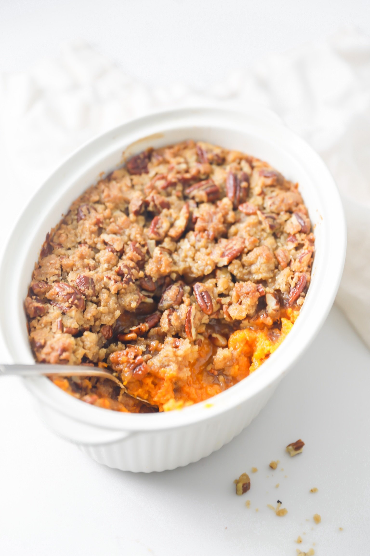 Sweet potato casserole with candied pecan topping in a white baking dish, fresh out of the oven.