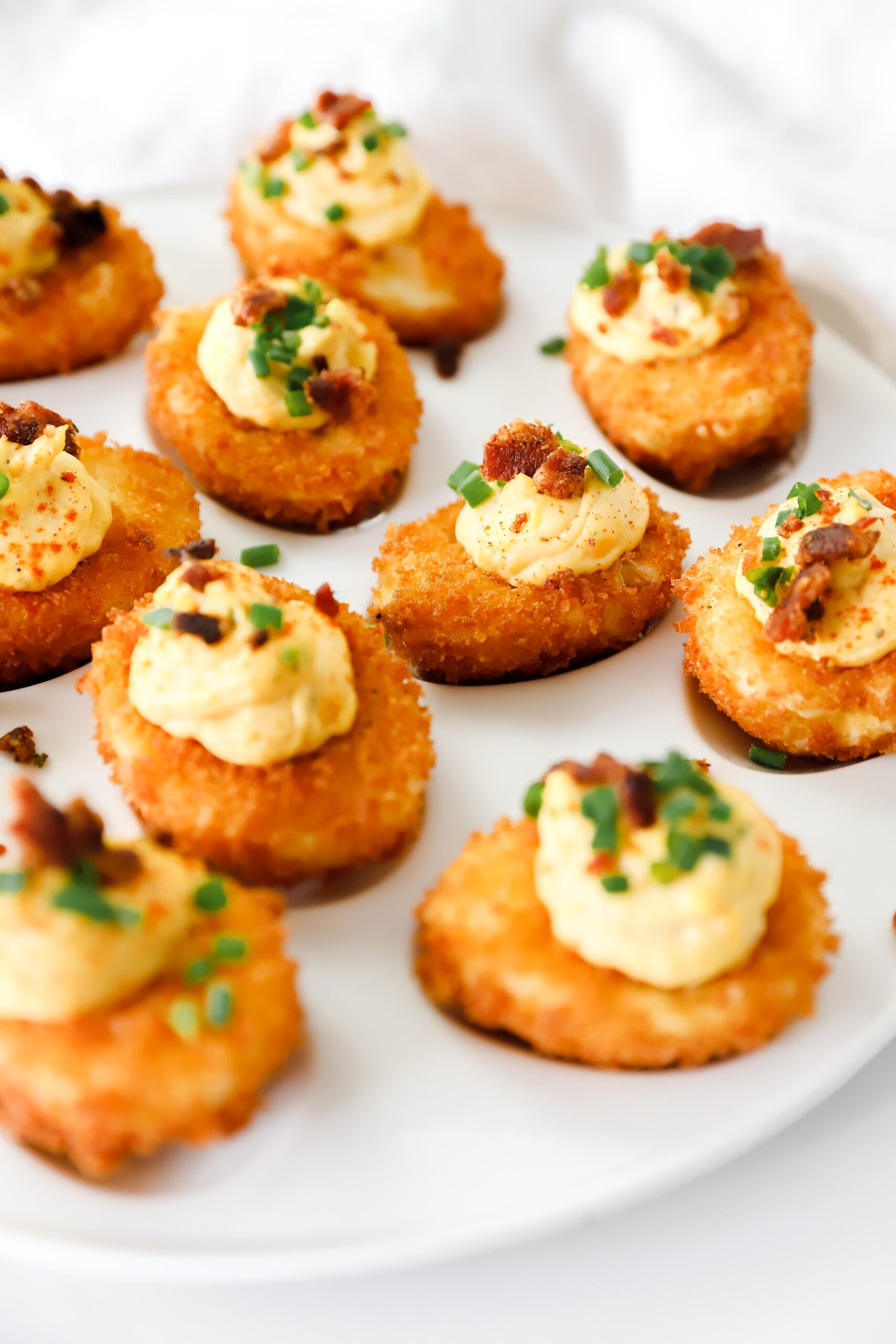 A plate of crispy fried deviled eggs topped with creamy filling, crispy bacon, and fresh chives, served on a rustic dish.