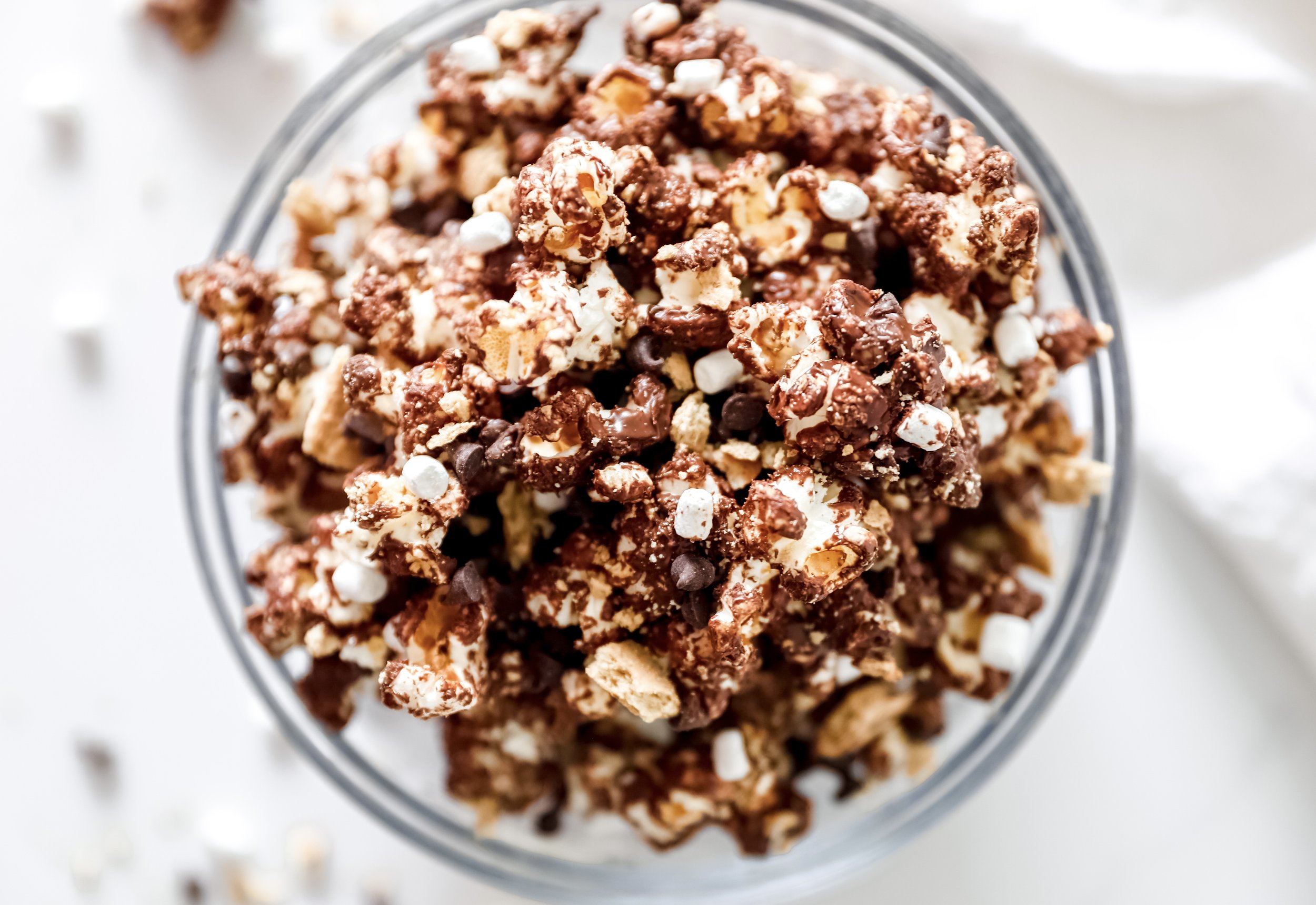 A large bowl of s’mores popcorn loaded with melted chocolate, graham cracker pieces, and mini marshmallows.