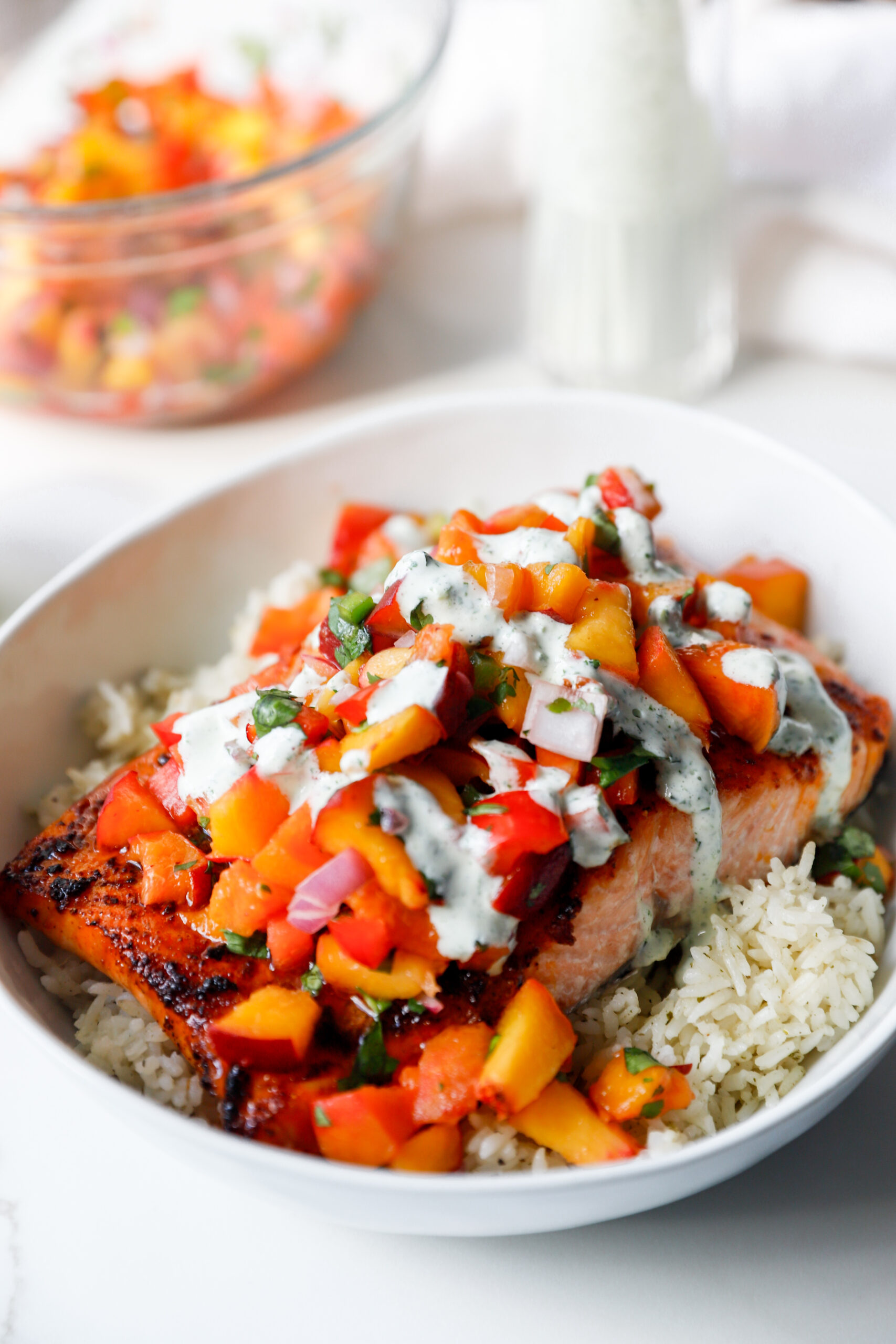 Close-up of flaky salmon topped with fresh peach salsa and cilantro crema over a bed of rice.