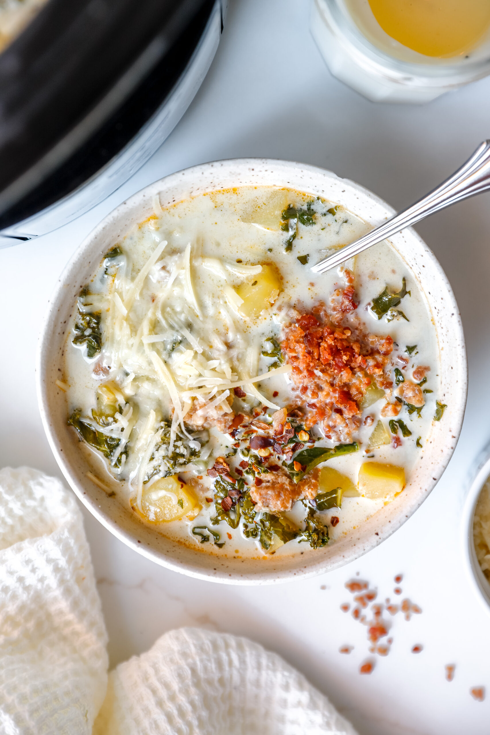 Bowl of Slow Cooker Zuppa Toscana topped with Parmesan and bacon bits on a marble countertop.