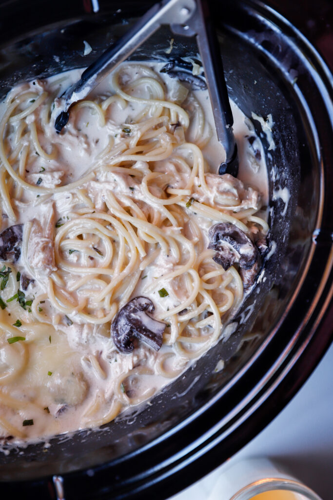 Overhead shot of slow cooker with twirled pasta in a creamy sauce with mushrooms and melted mozzarella cheese.