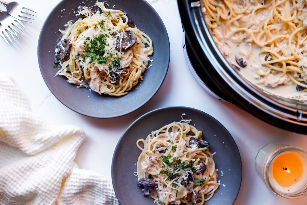 Overheat shot of 2 plates of creamy slow cooker chicken tetrazzini served on a black plate with parmesan and parsley next to the slow cooker