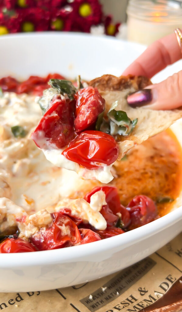 Close-up of a scoop of roasted tomatoes and creamy burrata on a slice of sourdough bread, topped with fresh basil and a drizzle of balsamic vinegar.