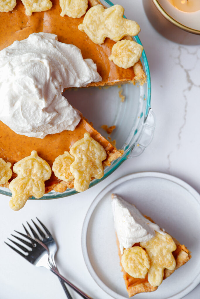 Decorated pumpkin pie with pie crust leaves and whipped cream, with a plated slice of pie on the side.
