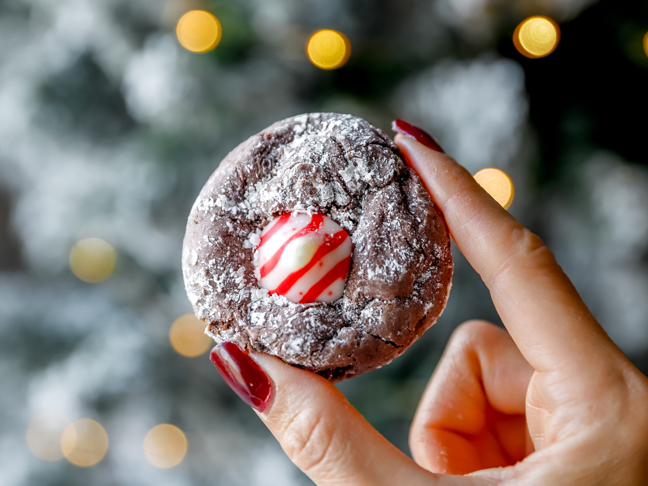 Close up of a hand holding a soft chocolate peppermint crinkle cookie topped with a Candy Cane Kiss.