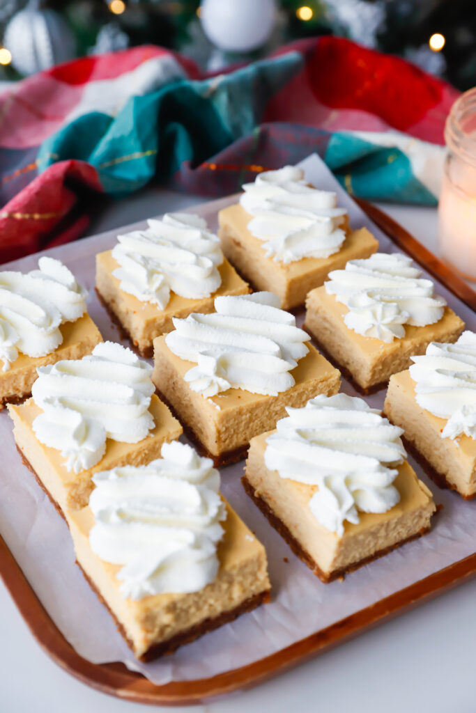 Angled shot of eggnog cheesecake bars arranged on a platter with whipped cream swirls.