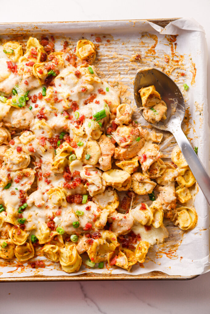 Overhead shot of sheet pan chicken bacon ranch tortellini with a serving spoon already dug into.