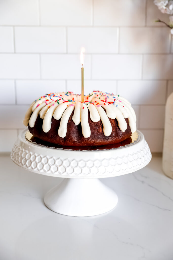 Chocolate bundt cake on a white cake pedestal with a lit candle.